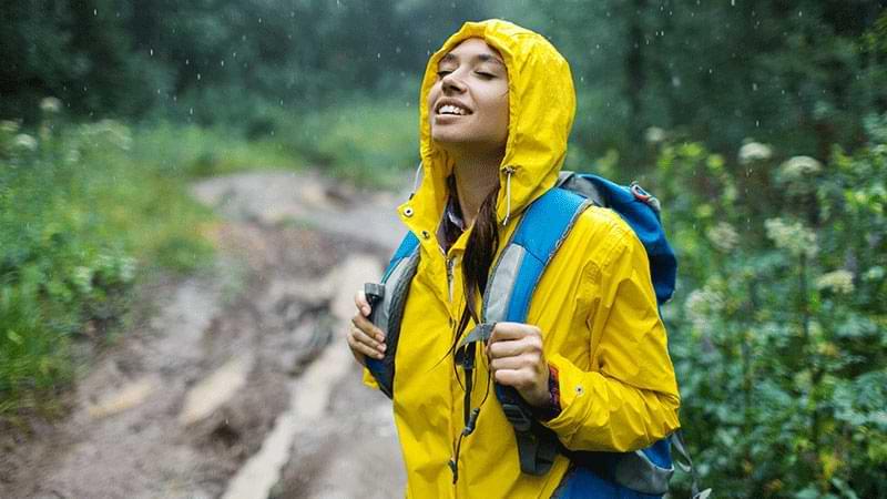 Young woman in raincoat enjoys nature in the rain